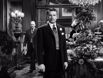 Movie still from “Carrie” (1952), directed by William Wyler – A black and white photo of a man in a suit and tie; Medium shot, Low angle