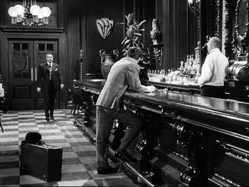 Movie still from “Carrie” (1952), directed by William Wyler – A man standing at the bar of an old fashioned cocktail bar; Wide shot, High angle
