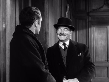 Movie still from “Carrie” (1952), directed by William Wyler – A man in a suit and hat shaking hands with another man in a hat; Medium shot, Over the shoulder angle