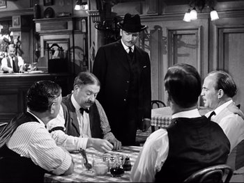 Movie still from “Carrie” (1952), directed by William Wyler – A group of men sitting at a table in front of a man in a hat; Medium shot, Over the shoulder angle