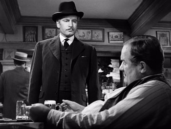 Movie still from “Carrie” (1952), directed by William Wyler – A man wearing a suit and a hat standing next to another man in a suit; Medium shot, Over the shoulder angle