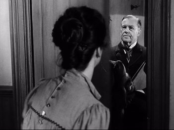 Movie still from “Carrie” (1952), directed by William Wyler – An older man and a young woman looking in the same mirror; Medium shot, Over the shoulder angle
