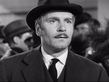 Movie still from “Carrie” (1952), directed by William Wyler – A man in a suit and a hat is standing in a crowd; Close Up shot, Low angle