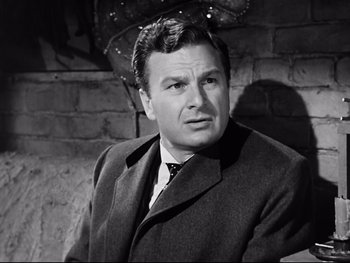 Movie still from “Carrie” (1952), directed by William Wyler – A man wearing a suit and tie standing in front of a brick wall; Close Up shot, Low angle