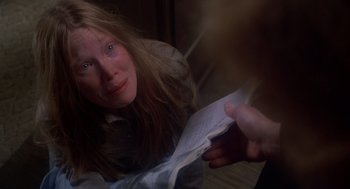 Movie still from “Carrie” (1976), directed by Brian De Palma – A woman is holding an open book while looking at the camera; Close Up shot, High angle