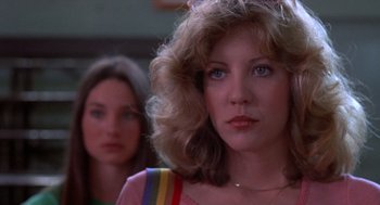 Movie still from “Carrie” (1976), directed by Brian De Palma – A woman with a rainbow colored shirt is looking at the camera while another woman stands in the background; Close Up shot, Low angle