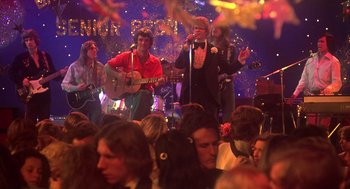 Movie still from “Carrie” (1976), directed by Brian De Palma – A group of people sitting in a room with a microphone; Wide shot, High angle