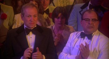 Movie still from “Carrie” (1976), directed by Brian De Palma – A group of people sitting in front of each other clapping; Medium shot, Over the shoulder angle