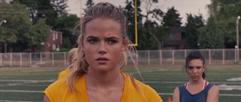 Movie still from “Carrie” (2013), directed by Kimberly Peirce – A woman in a yellow shirt is standing on a football field; Close Up shot, Over the shoulder angle