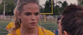 Movie still from “Carrie” (2013), directed by Kimberly Peirce – A woman in a yellow shirt is standing on a field; Close Up shot, Over the shoulder angle