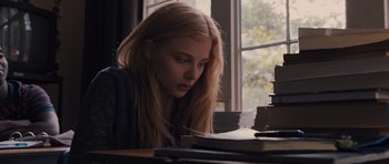 Movie still from “Carrie” (2013), directed by Kimberly Peirce – A woman sitting at a table with a stack of books; Medium shot, Low angle