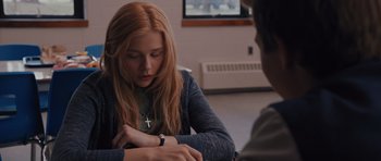 Movie still from “Carrie” (2013), directed by Kimberly Peirce – A woman sitting in front of a man with a cross on her neck; Medium shot, Over the shoulder angle