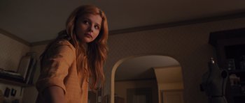 Movie still from “Carrie” (2013), directed by Kimberly Peirce – A woman with long red hair standing in front of a mirror; Medium shot, Low angle