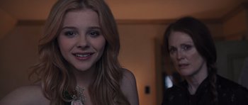 Movie still from “Carrie” (2013), directed by Kimberly Peirce – A woman with a flower in her hair and another woman with a flower in her hand; Close Up shot, Over the shoulder angle