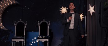 Movie still from “Carrie” (2013), directed by Kimberly Peirce – A man in a suit and tie holding a microphone; Medium shot, Low angle