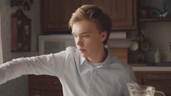 Movie still from “The Clovehitch Killer” (2018), directed by Duncan Skiles – A young man in a blue dress shirt is standing in front of a kitchen counter; Close Up shot, Low angle