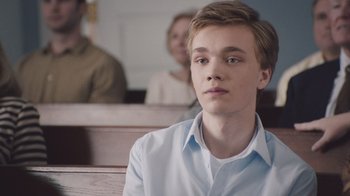Movie still from “The Clovehitch Killer” (2018), directed by Duncan Skiles – A young man sitting in front of a group of people; Close Up shot, Over the shoulder angle