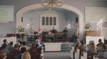 Movie still from “The Clovehitch Killer” (2018), directed by Duncan Skiles – A group of people in a church singing and playing instruments; Wide shot, High angle
