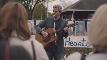 Movie still from “The Clovehitch Killer” (2018), directed by Duncan Skiles – A man in a suit playing a guitar in front of a crowd; Medium shot, Over the shoulder angle