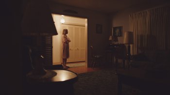 Movie still from “The Clovehitch Killer” (2018), directed by Duncan Skiles – A woman standing in front of an open door in a living room; Wide shot, Low angle