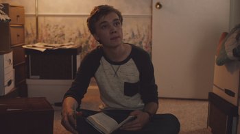 Movie still from “The Clovehitch Killer” (2018), directed by Duncan Skiles – A man sitting on the floor holding a book; Medium shot, Over the shoulder angle