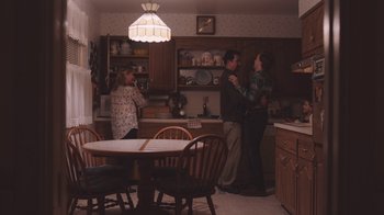 Movie still from “The Clovehitch Killer” (2018), directed by Duncan Skiles – A group of people standing in a kitchen next to a table; Wide shot, Over the shoulder angle