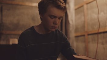 Movie still from “The Clovehitch Killer” (2018), directed by Duncan Skiles – A young man sitting in front of an open book; Close Up shot, High angle