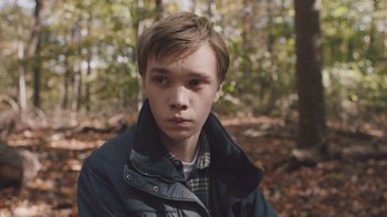Movie still from “The Clovehitch Killer” (2018), directed by Duncan Skiles – A young man in a jacket in the woods; Close Up shot, High angle