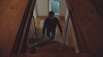 Movie still from “The Clovehitch Killer” (2018), directed by Duncan Skiles – A man walking up the stairs in a house; Wide shot, Low angle
