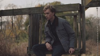Movie still from “The Clovehitch Killer” (2018), directed by Duncan Skiles – A man sitting on top of a wooden bench outside; Medium shot, Low angle