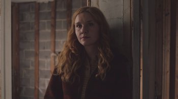 Movie still from “The Clovehitch Killer” (2018), directed by Duncan Skiles – A woman with long red hair standing in a room; Medium shot, Low angle