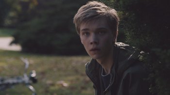 Movie still from “The Clovehitch Killer” (2018), directed by Duncan Skiles – A young man is sitting in the grass looking at the camera; Close Up shot, Over the shoulder angle