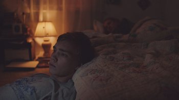 Movie still from “The Clovehitch Killer” (2018), directed by Duncan Skiles – A man laying in a bed next to a woman; Medium shot, High angle