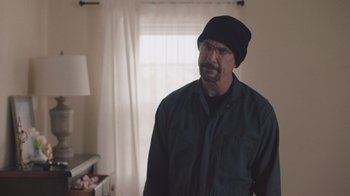 Movie still from “The Clovehitch Killer” (2018), directed by Duncan Skiles – A man wearing a hat standing in front of a window; Medium shot, Over the shoulder angle