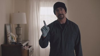 Movie still from “The Clovehitch Killer” (2018), directed by Duncan Skiles – A man in a black jacket and a black hat is holding up a finger; Medium shot, Low angle