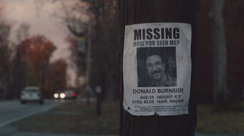 Movie still from “The Clovehitch Killer” (2018), directed by Duncan Skiles – A missing person poster hanging on the side of a telephone pole; Wide shot, High angle