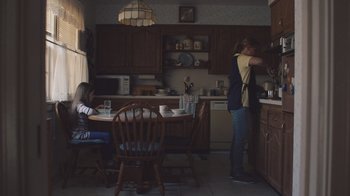 Movie still from “The Clovehitch Killer” (2018), directed by Duncan Skiles – Two people in a kitchen with a table and chairs; Wide shot, Low angle