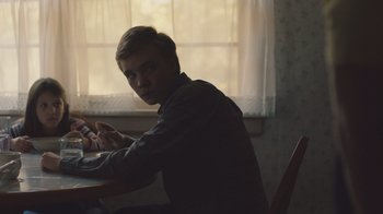 Movie still from “The Clovehitch Killer” (2018), directed by Duncan Skiles – A man sitting at a dining room table in front of a window; Medium shot, Over the shoulder angle