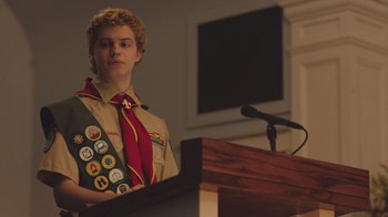 Movie still from “The Clovehitch Killer” (2018), directed by Duncan Skiles – A boy scout standing in front of a microphone; Medium shot, Low angle