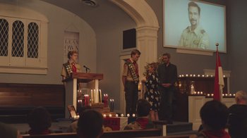 Movie still from “The Clovehitch Killer” (2018), directed by Duncan Skiles – A group of people standing in front of a podium; Wide shot, Over the shoulder angle