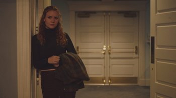 Movie still from “The Clovehitch Killer” (2018), directed by Duncan Skiles – A woman holding a jacket in front of a garage door; Medium shot, Low angle