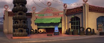 Movie still from “Cars 3” (2017), directed by Brian Fee – A cartoon scene of a tire shop with a car parked in front of it; Wide shot, Low angle