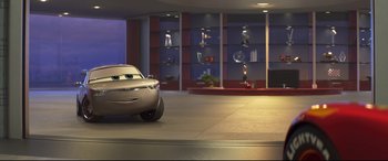 Movie still from “Cars 3” (2017), directed by Brian Fee – A car parked in front of a building with shelves; Wide shot, Low angle