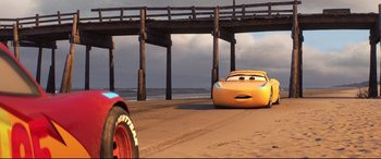 Movie still from “Cars 3” (2017), directed by Brian Fee – A yellow car driving down a road next to a pier; Wide shot, Low angle