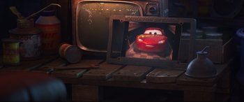 Movie still from “Cars 3” (2017), directed by Brian Fee – A picture of a car on a wooden table next to an old tv; Wide shot, Over the shoulder angle
