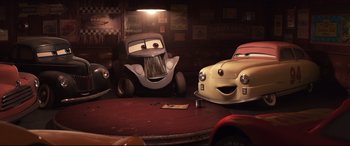 Movie still from “Cars 3” (2017), directed by Brian Fee – A couple of cars that are sitting in a room together; Wide shot, Low angle