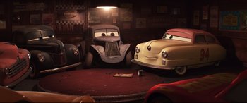 Movie still from “Cars 3” (2017), directed by Brian Fee – A couple of cars that are sitting in a room together; Wide shot, Low angle