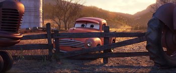 Movie still from “Cars 3” (2017), directed by Brian Fee – An orange truck is behind a wooden fence in a field; Wide shot, Low angle