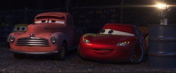 Movie still from “Cars 3” (2017), directed by Brian Fee – A red truck and a red car in a parking lot at night; Wide shot, High angle