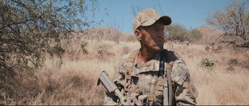 Movie still from “Cartel Land” (2015), directed by Matthew Heineman – A man in camouflage holding a rifle in a field; Close Up shot, Over the shoulder angle